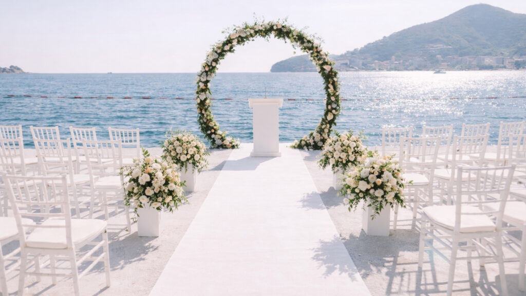 Seaside wedding ceremony with a white aisle runner, floral arch, and white chairs arranged along the oceanfront