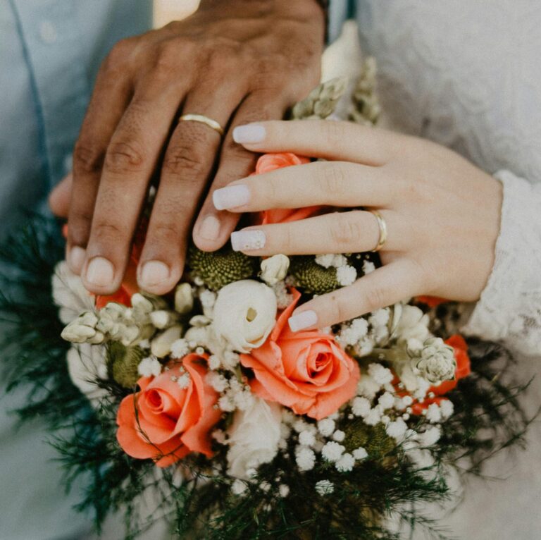 Hands of the bride and groom with wedding rings and floral bouquet, symbolizing love and commitment.