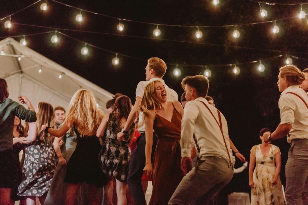A lively outdoor night party with people dancing under string lights.