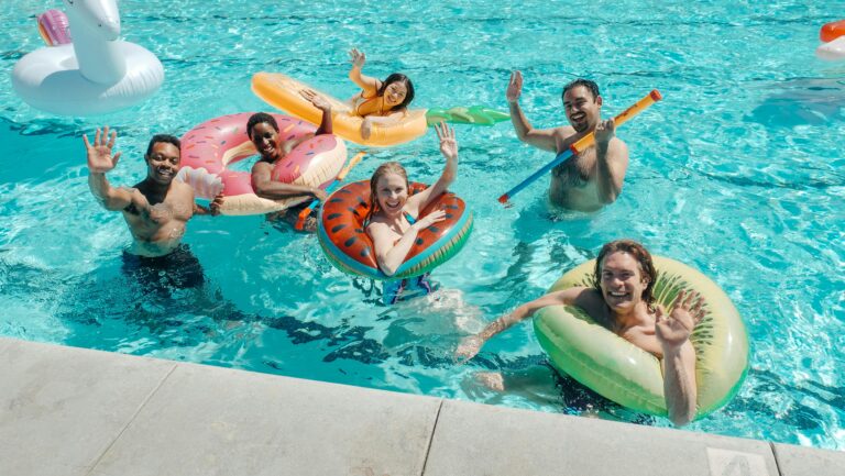 A diverse group of friends waving and having fun at a lively summer wedding pool party.