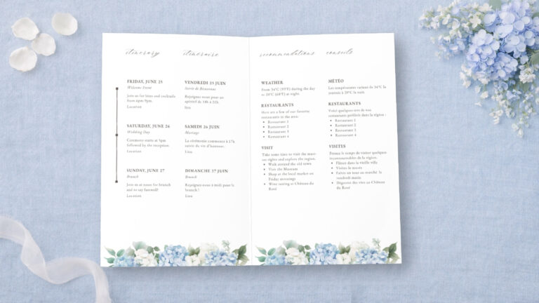 Flat lay of bilingual wedding weekend itinerary cards on blue linen with silk ribbon and blue florals with baby’s breath, styled for a destination wedding welcome suite.