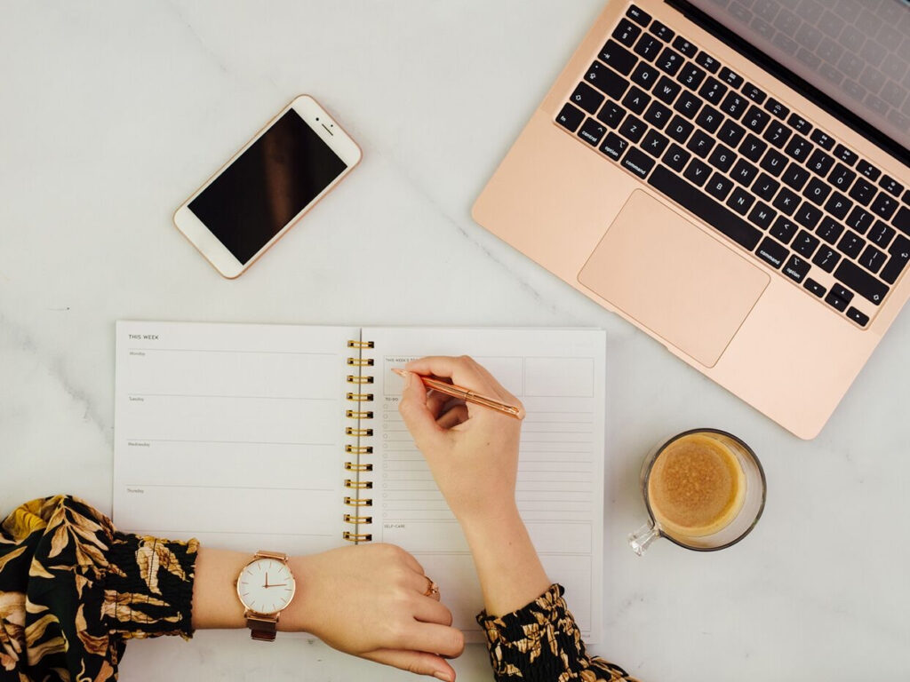 bride sitting at desk planning destination wedding with laptop, notebook, and coffee.